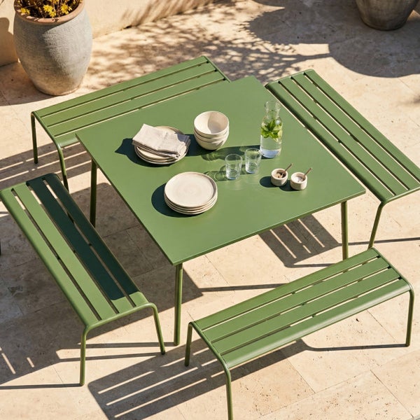 Quadratischer Gartentisch aus Metall mit vier passenden Gartenbänken auf einer hellen Steinterrasse.