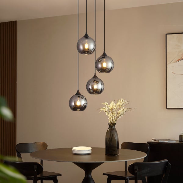 Moderne vierflammige Pendelleuchte mit gläsernen Kugelschirmen über einem runden Esstisch in einem wohnlichen Esszimmer.