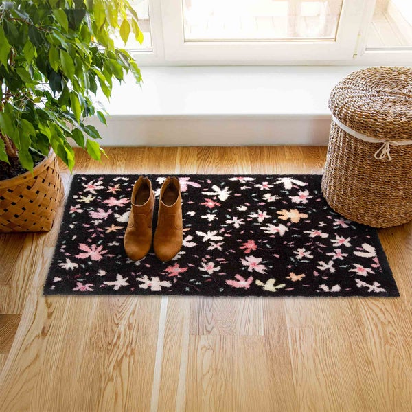 Schwarze Fußmatte mit Blumenmuster, Schuhen und Pflanze in Korb