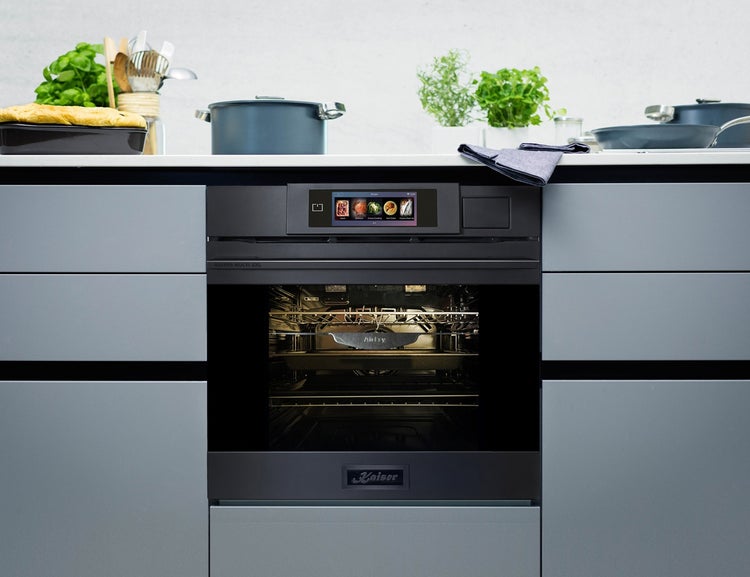 Kaiser Einbaubackofen mit Touchdisplay, integriert in eine moderne Küchenzeile mit Arbeitsplatte und Kochutensilien.