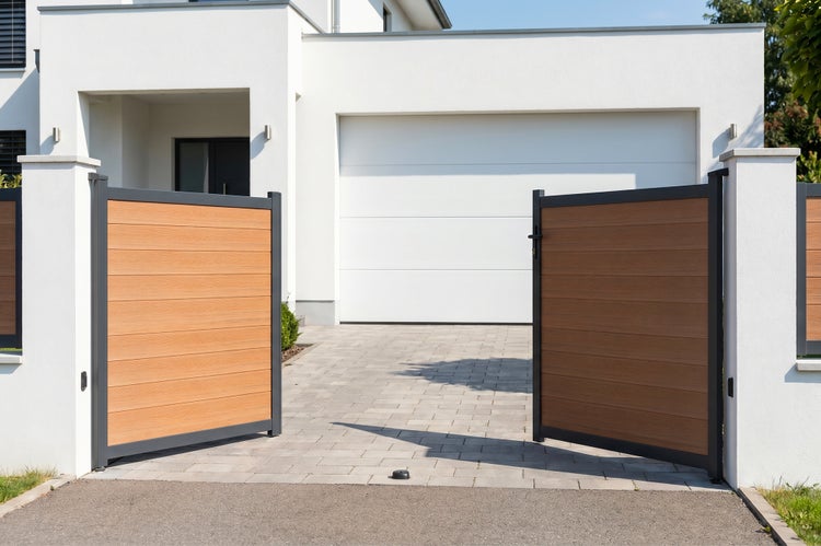 Zweiflügeliges Einfahrtstor mit anthrazitfarbenem Metallrahmen und horizontalen Paneelen in Holzoptik vor einem modernen Wohnhaus.