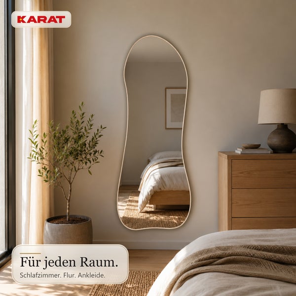 Großer Wandspiegel mit organischer Form in einem modern eingerichteten Schlafzimmer mit Holzkommode und Pflanze. Karat Logo.
