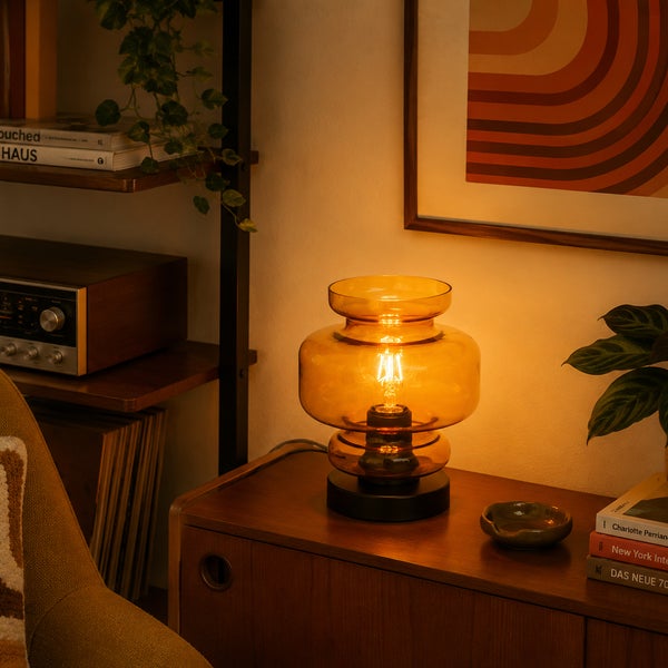 Tischleuchte mit gläsernem Lampenschirm in Mid Century Optik auf einem hölzernen Sideboard in einem gemütlich eingerichteten Wohnbereich.