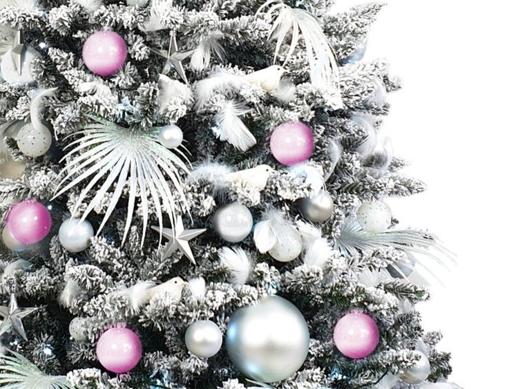 Detailansicht eines künstlichen, verschneiten Weihnachtsbaums, geschmückt mit Kugeln, Sternen, Federn und Vogeldekorationen.