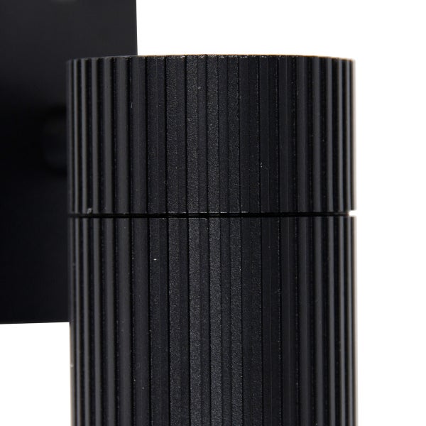 Detailaufnahme einer schwarzen, zylindrischen Wandleuchte mit vertikal geriffelter Oberflächenstruktur.