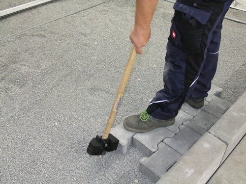 Eine Person verwendet einen Gummihammer, um Pflastersteine zu verlegen.