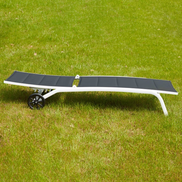 Sonnenliege mit weißem Metallgestell, dunkelgrauer Textilbespannung und Rollen auf grünem Rasen.