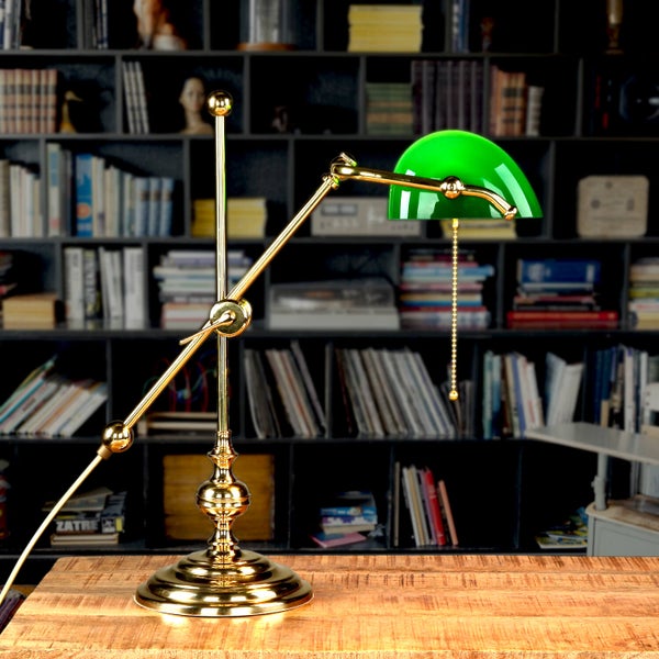 Grüne Bankerlampe mit goldenem Gestell auf einem Holztisch vor einem Bücherregal