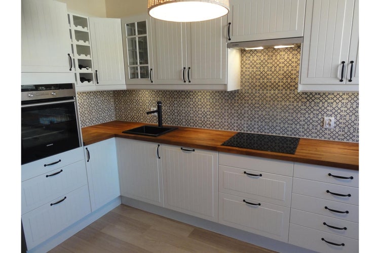 Helle Küche mit weißen Schränken, Holzarbeitsplatten und dunklen Beschlägen.