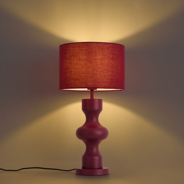 Rote Tischleuchte mit geschwungenem Fuß und Stoffschirm, eingeschaltet mit warmem Lichtkegel nach oben und unten.