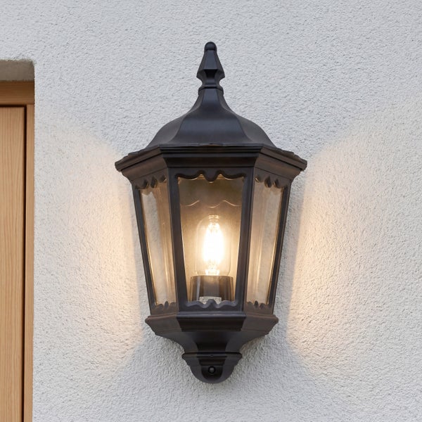Klassische Außenwandleuchte in Laternenform an einer Hauswand, beleuchtet mit warmem Licht.