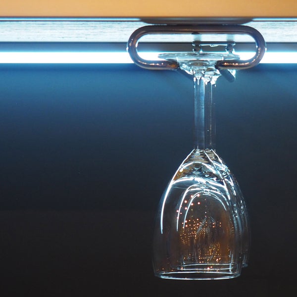 Weinglas in einem Metallhalter, der unter einem Schrank mit LED-Beleuchtung montiert ist.