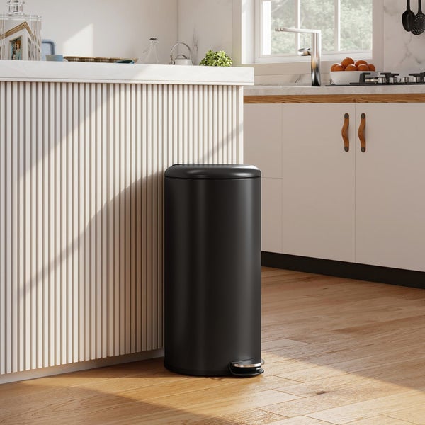 Schwarzer Tretmülleimer in einer hellen, modernen Küche neben einer Kücheninsel auf Holzboden.