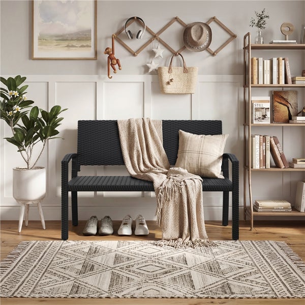 Schwarze Gartenbank aus Polyrattan in hellem Raum mit gemustertem Teppich, Zimmerpflanze und Wandgarderobe aus Holz.