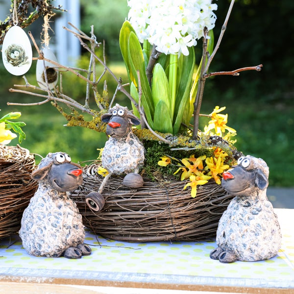 Dekorative Osterdekoration mit Keramikschafen und Frühlingsblumen im Korb