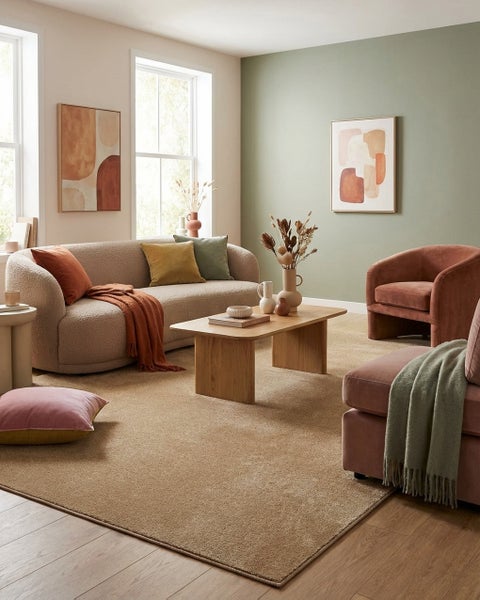 Helles Wohnzimmer mit beigem Sofa, Holztisch, zwei Sesseln und einem großen Teppich auf Parkettboden.