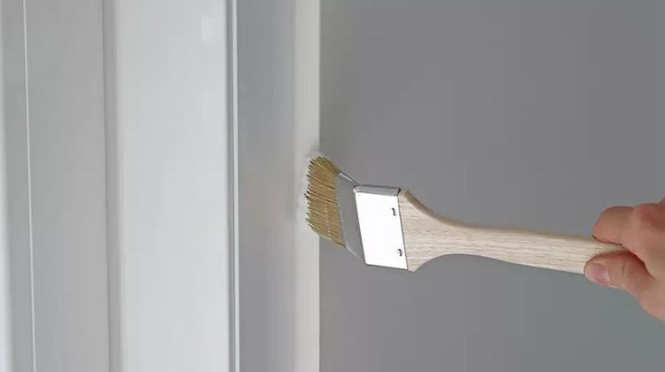 Ein Heizkörperpinsel mit Holzstiel trägt weiße Farbe an die Kante eines Rahmens auf.