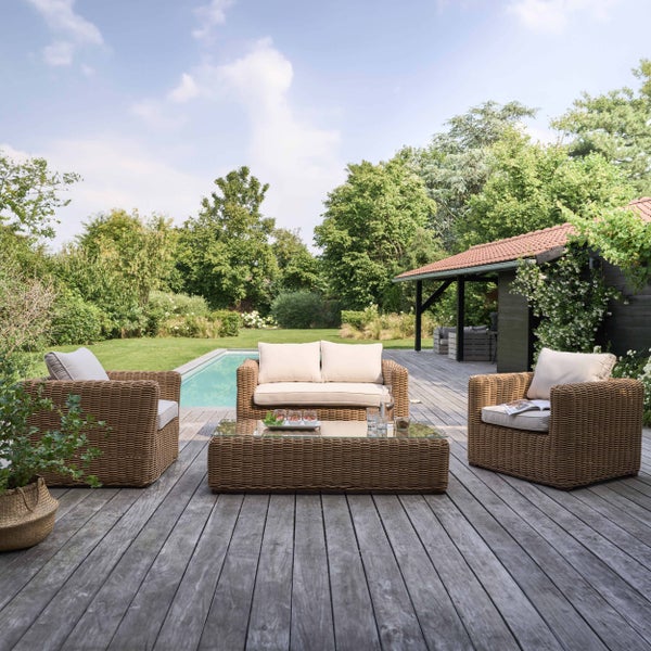 Geflochtenes Lounge-Set bestehend aus zwei Sesseln, einem Sofa und einem Tisch auf einer Holzterrasse neben einem Pool und Garten.