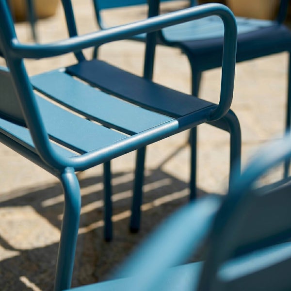 Blaue Gartenstühle aus Metall mit Armlehnen und einer Sitzfläche aus Lamellen.
