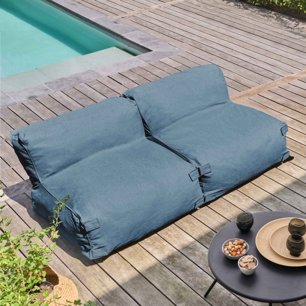 Blaues Outdoor-Sitzsack-Sofa aus Textil auf einer hellen Holzterrasse am Pool mit Beistelltisch in einer modernen, hellen Gartenanlage.