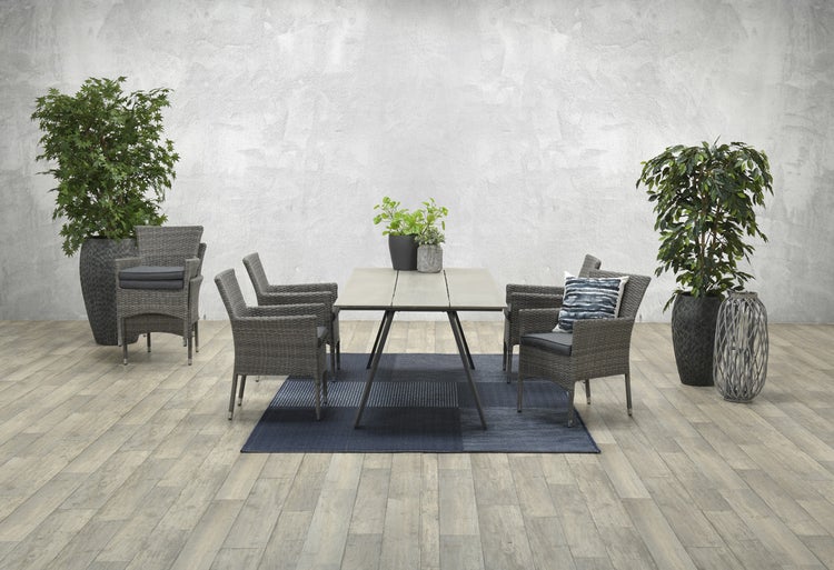 Moderne Garten-Sitzgruppe mit rechteckigem Tisch und sechs grauen Geflechtstühlen inklusive Sitzkissen auf einem blauen Teppich.