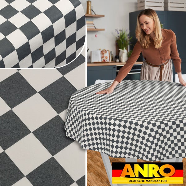 Eine Frau glättet eine runde, karierte Wachstuch-Tischdecke auf einem Tisch in einer hellen Küche, Detailansicht der Struktur, ANRO Logo.