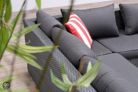 Detail eines grauen Garten-Loungesofas aus Polyrattan mit Sitzkissen und einem rot-weiß gestreiften Dekokissen hinter grünen Blättern.