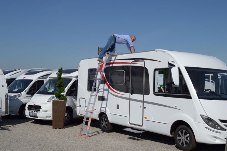 Mann auf dem Dach eines Wohnmobils mit einer Mehrzweckleiter.