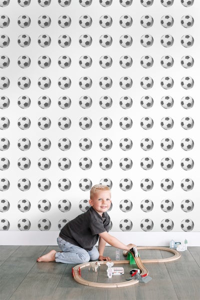 Junge spielt mit Holzeisenbahn vor einer Wand mit Fussballtapete