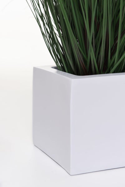 Künstliche Pflanze Gras in einem weißen quadratischen Übertopf.