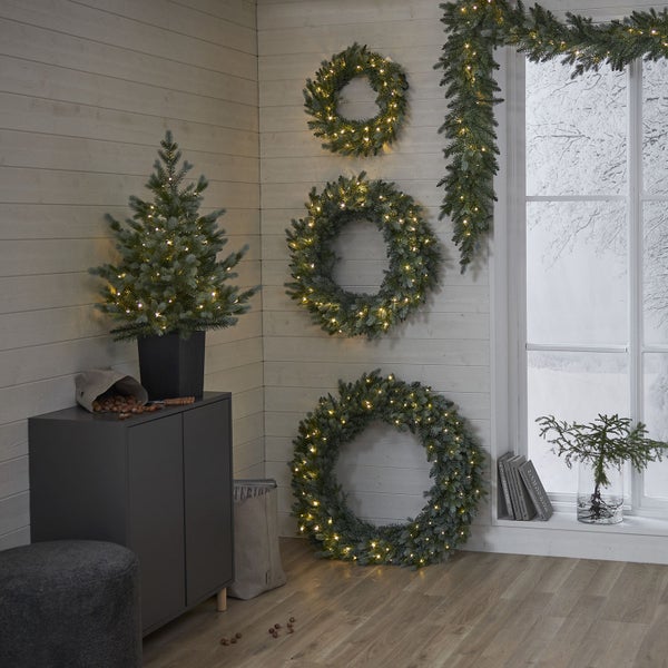 Winterliche Raumdekoration mit beleuchteten Kränzen, Girlande und kleinem Weihnachtsbaum auf einem grauen Schrank