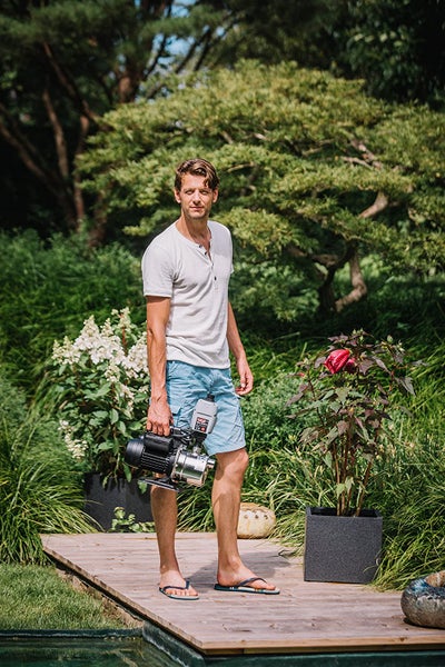 Mann trägt Gartenpumpe im Garten auf Holzterrasse