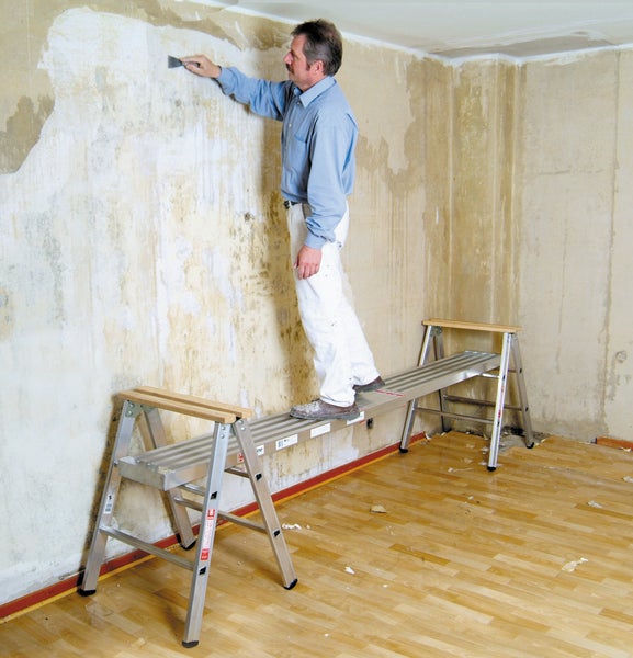 Handwerker auf einer Arbeitsbühne beim Entfernen alter Tapeten von einer Wand.