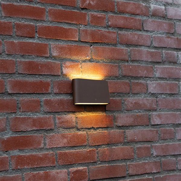 Dunkelbraune, rechteckige Außenwandleuchte an einer Ziegelwand mit Lichtaustritt nach oben und unten.