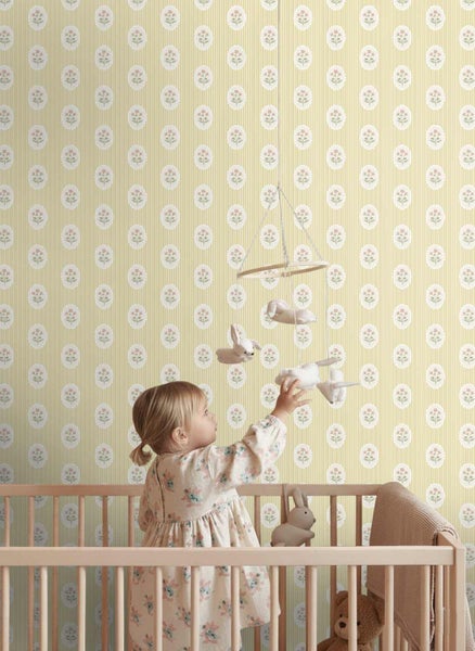 Klassische Kindertapete mit Längsstreifen und floralen Medaillons in einem hellen Kinderzimmer hinter einem Gitterbett aus Holz.