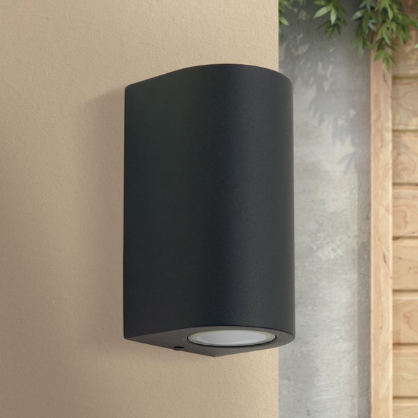 Schwarze matte Außenwandleuchte in abgerundeter Form an einer Hauswand.