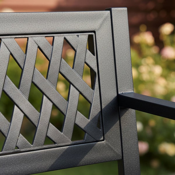 Schwarze Gartenbank aus Metall mit Rautenmuster in einem Garten mit einem Mann und einem Hund.
