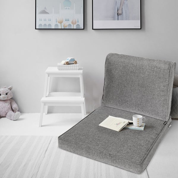 Gepolsterter Bodenstuhl in Grau in einem hellen Kinderzimmer mit weißem Tritthocker aus Holz, Stofftier und Teppich.