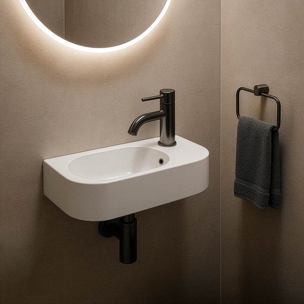 Modernes Gäste-WC mit weißem Keramik-Handwaschbecken, dunkler Armatur und Siphon sowie einem runden beleuchteten Spiegel.