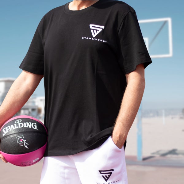 Person mit schwarzem T-Shirt und weißen Shorts, hält einen Spalding Basketball