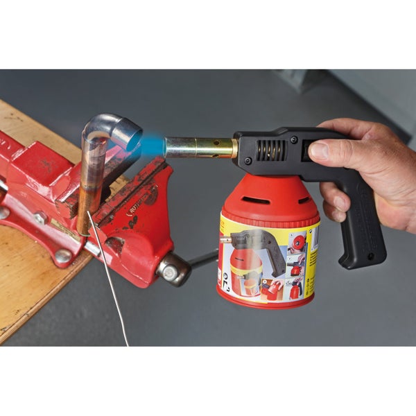 Hand führt Lötbrenner mit blauer Flamme an ein in einem Schraubstock eingespanntes Kupferrohr zum Weichlöten.