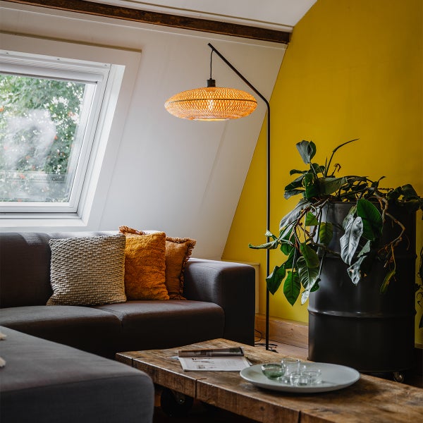 Wohnzimmer mit Sofa, Holztisch, Stehlampe und Zimmerpflanze in einem Fass