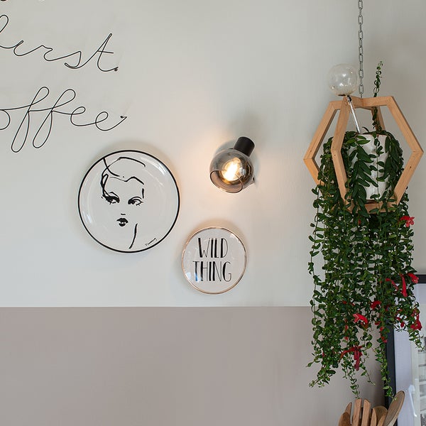 Wanddekoration mit Teller, Lampe und Hängepflanze im Holzrahmen