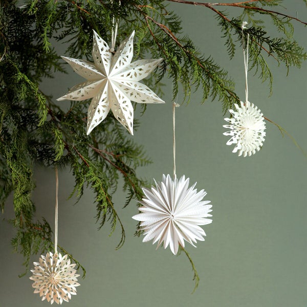 Set mit vier dekorativen Weihnachtssternen und Schneeflocken aus Papier, hängend an einem Tannenzweig zur winterlichen Dekoration.