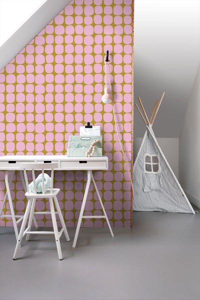 Vliestapete mit geometrischem Muster aus rosa abgerundeten Quadraten auf olivgrünem Grund in einem Kinderzimmer mit weißem Schreibtisch.