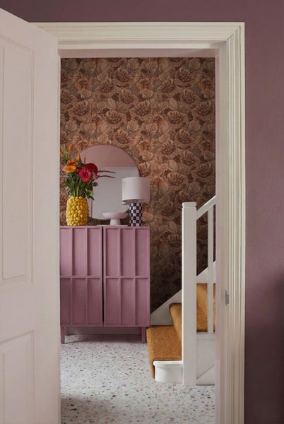 Blick durch eine geöffnete Tür auf einen Flur mit Kommode, Blumenstrauß und Treppe