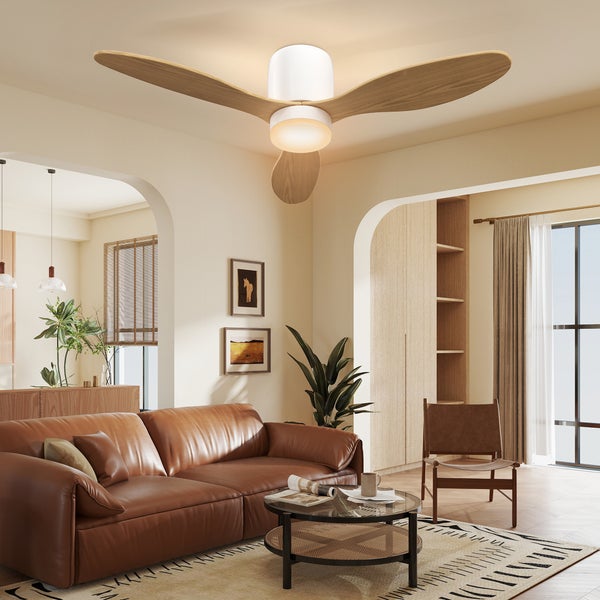 Deckenventilator mit drei Holzflügeln und Leuchte in einem hellen Wohnzimmer mit braunem Ledersofa, Holzmöbeln und Pflanzen.