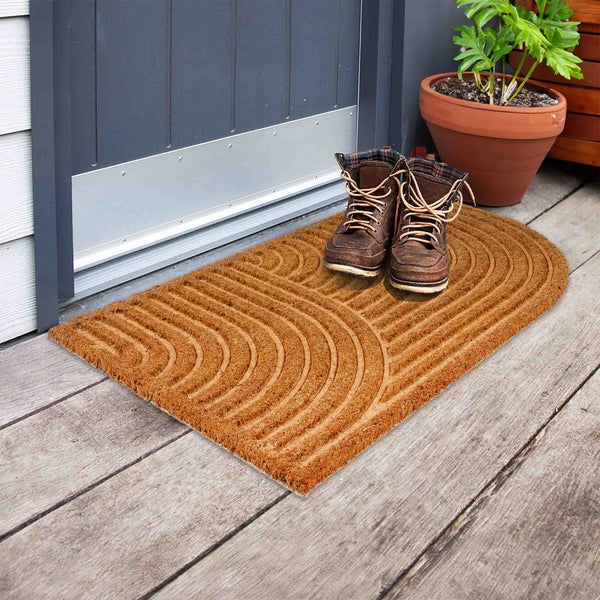 Fußmatte aus Kokosfaser mit Muster vor einer Haustür mit Stiefeln