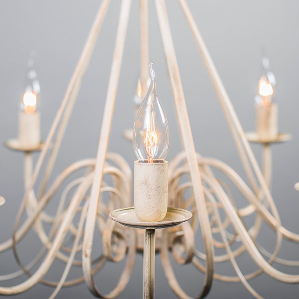 Detailaufnahme eines cremefarbenen Kronleuchters mit filigranen Armen und tropfenförmigen Leuchtmitteln