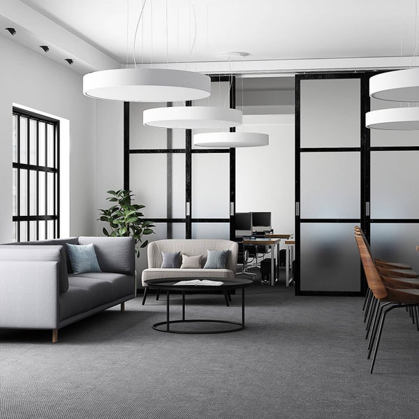 Moderner Loungebereich im Büro mit grauen Sofas, schwarzem Couchtisch, großen weißen Pendelleuchten und industriellen Glastrennwänden.